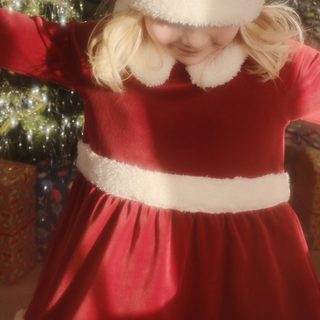 Child wearing a red dress with white trim in front of a Christmas tree.