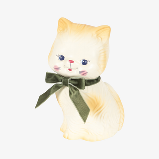 A cream-colored  cat money bank with a dark green velvet bow around its neck, set against a plain light gray background.