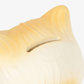 A close up of the coin slot on a cream-colored cat money bank, set against a plain light gray background.