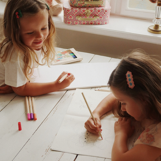 Two young girls drawing at a table with art supplies.