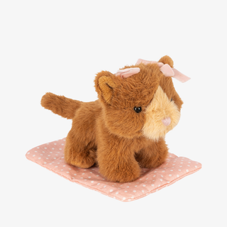 A brown plush toy cat with pink bows in its ears, sitting on a pink polka-dot cushion against a plain white background.