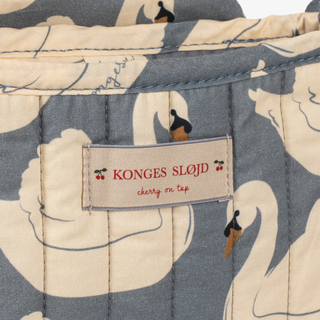 Close-up of a quilted fabric product with a cream and slate blue floral print, featuring a sewn-in label that reads 'KONGES SLOJD cherry on top'.