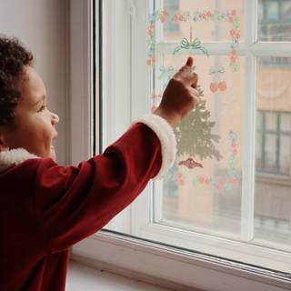 Child in a red coat decorating a window with festive stickers.