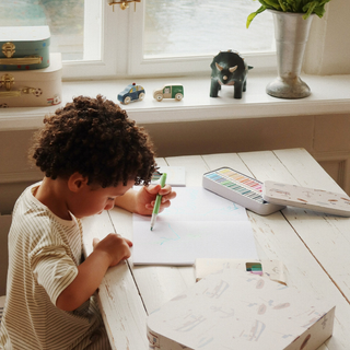 Child drawing at a table with art supplies and toys in the background