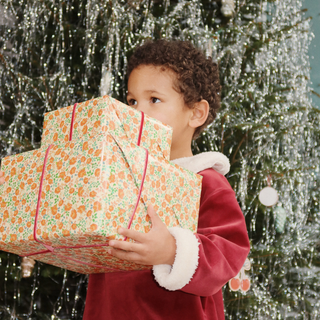 Child holding a large gift box in front of a decorated Christmas tree