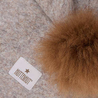 Brown fur pom-pom on a textured fabric background with a visible brand label.