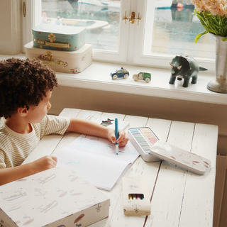 Child drawing at a desk with toys and stationery around