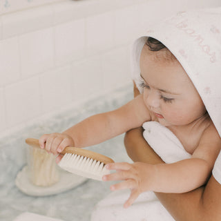 Baby in a hooded towel playing with a brush