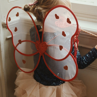 Child wearing butterfly wings with red accents indoors