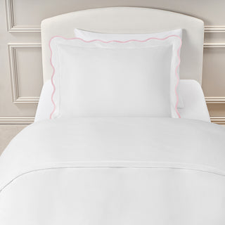 White bedding set with pink trim on a bed against a neutral wall.