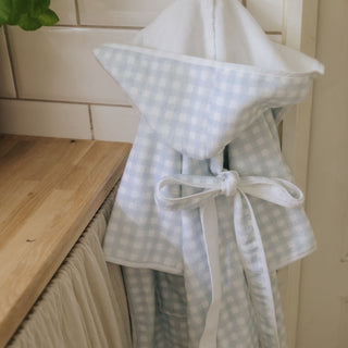 Light blue checkered bathrobe with a white hood and tie, hanging on a wooden surface.