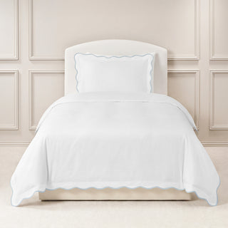 White comforter with scalloped edges on a bed against a blue paneled wall.