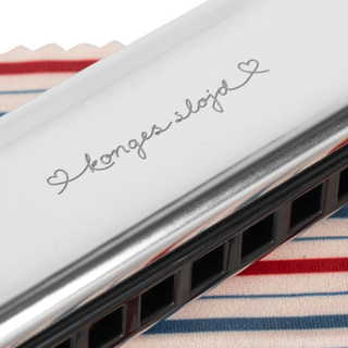 Metallic harmonica with 'Konges Slojde' branding on a striped fabric background