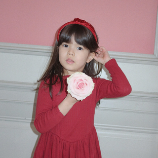 Young girl in a red dress holding a pink flower against a pink wall.