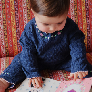 Child wearing a blue sweater with floral patterns, sitting on a colorful patterned couch.