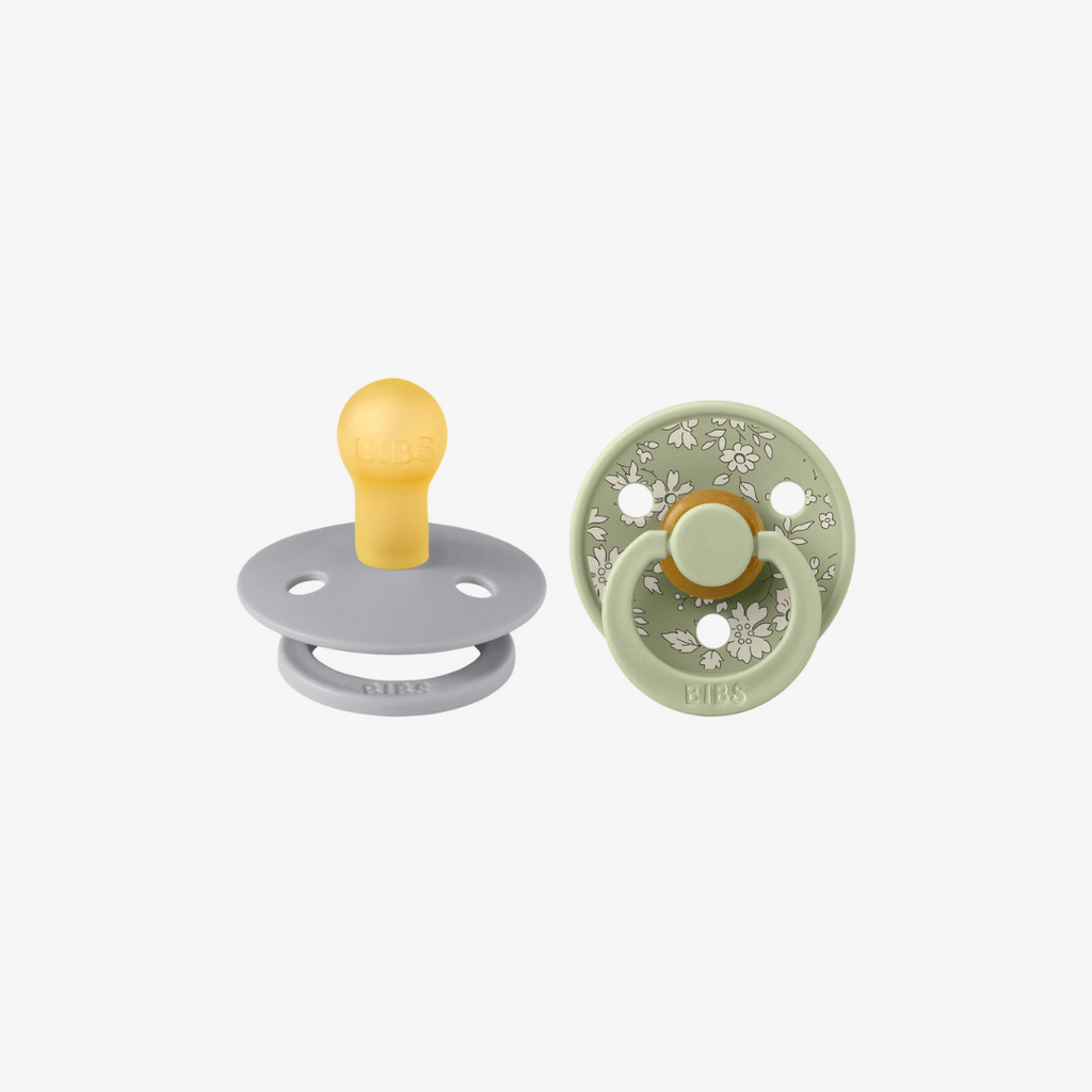 Two baby pacifiers, one gray and one green with floral design, on a white background.