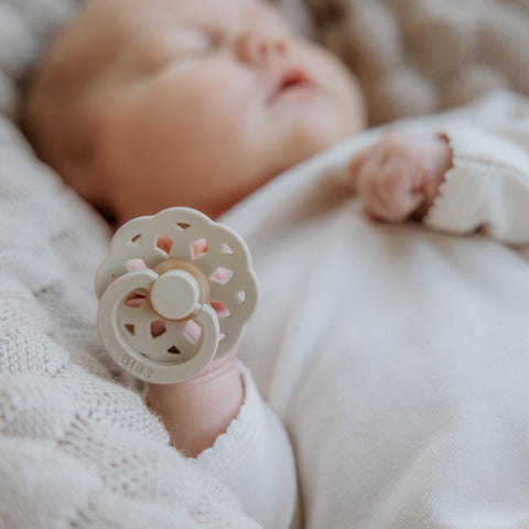 Baby holding a floral pacifier with a soft focus background