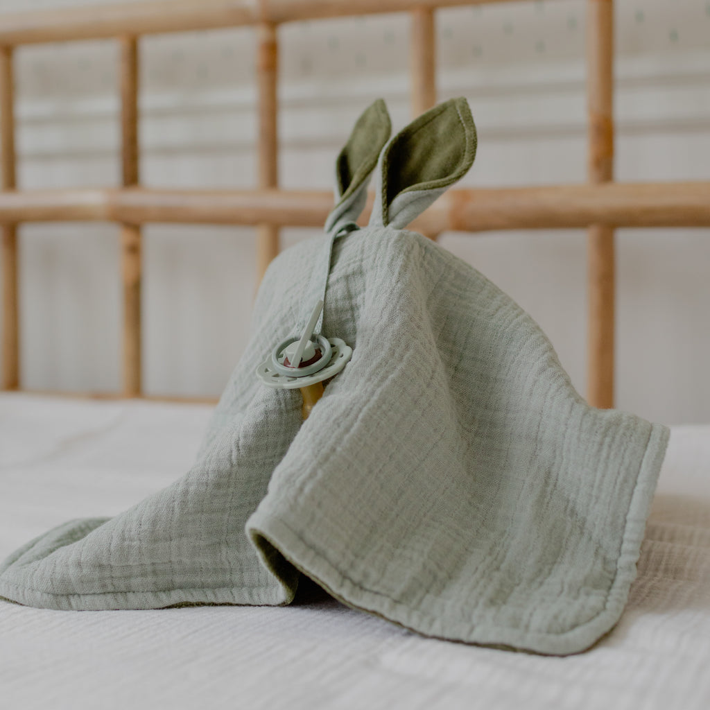 Green baby blanket shaped like a bunny with rabbit ears on a bed.
