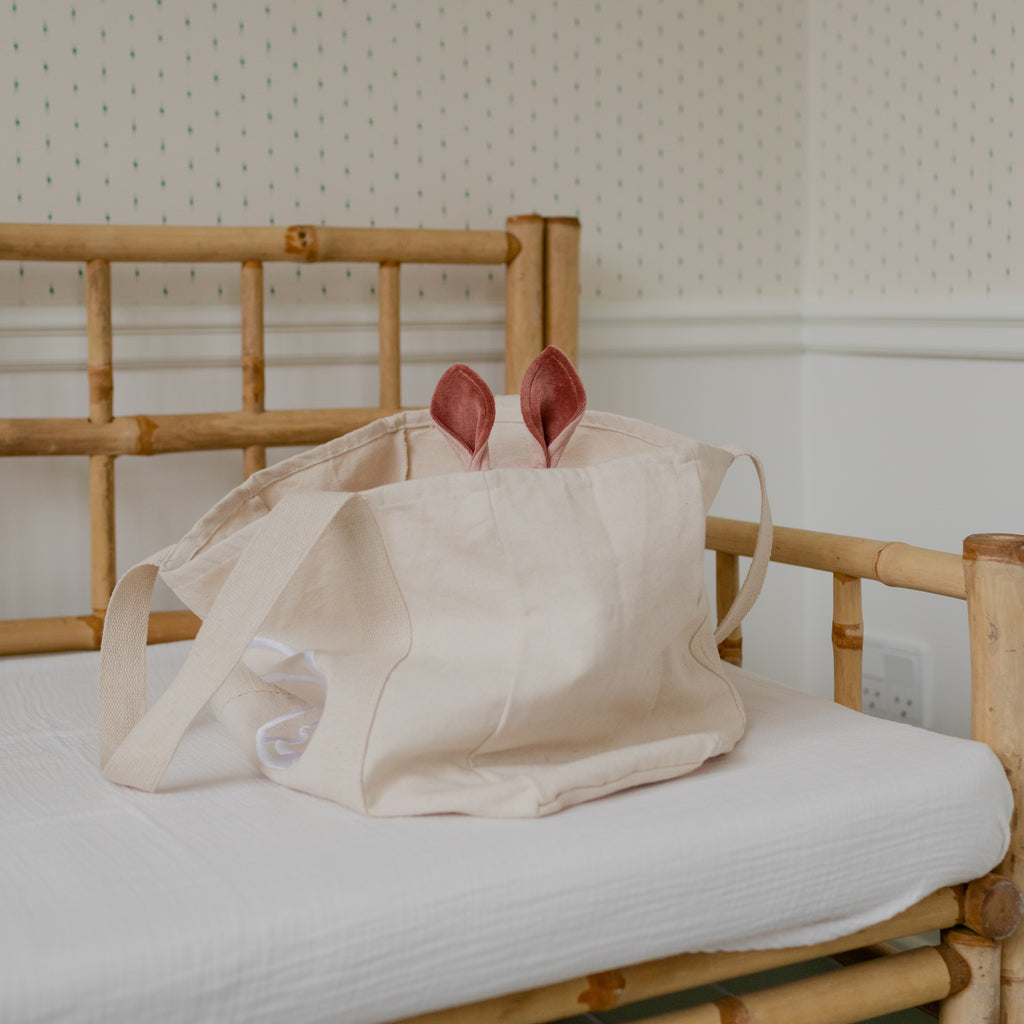 Beige tote bag with pink items on a wooden chair against a white wall.