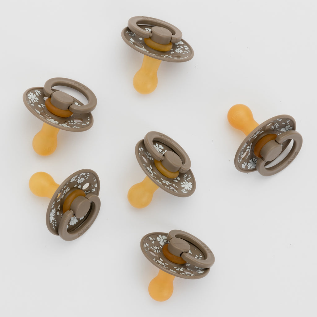 Set of six baby pacifiers with decorative metal rings on a white background