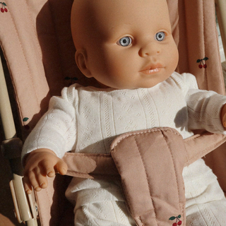Baby doll in a white outfit with a pink carrier against a soft, blurred background