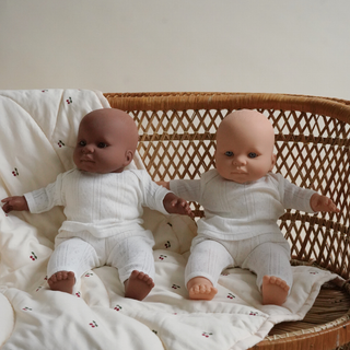 Two dolls in white outfits sitting on a textured surface with a wicker basket in the background.