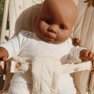 Baby doll wearing a white outfit with buttons, sitting in a wooden crib.