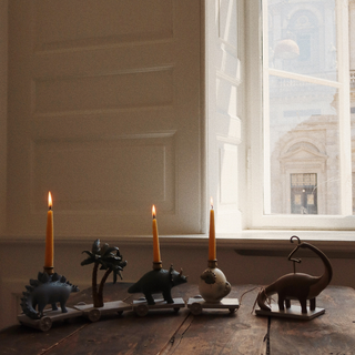 Decorative candle holders shaped like dinosaurs on a wooden surface near a window.
