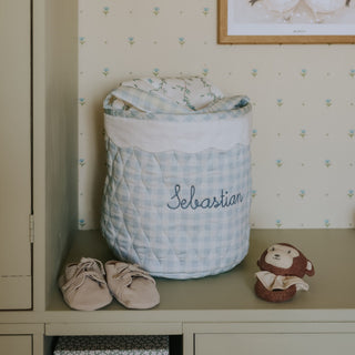 Quilted baby storage basket with 'Sebastian' on a shelf with baby shoes and a monkey toy.