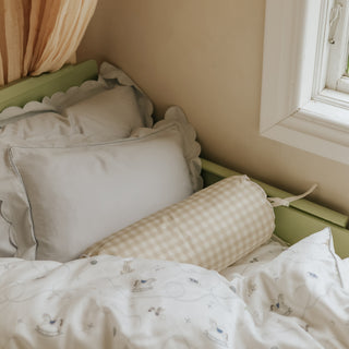 Bed with pillows and a picnic gingham beige bolster against a window in a room. 