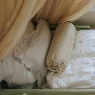 Close-up of a crib with picnic gingham beige bolster pillow and a patterned blanket.