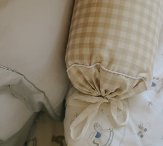 picnic gingham beige bolster pillow with tied ends on a bed with white bedding.