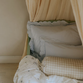Bed with green headboard, beige curtains, and picnic gingham beige bolster pillow