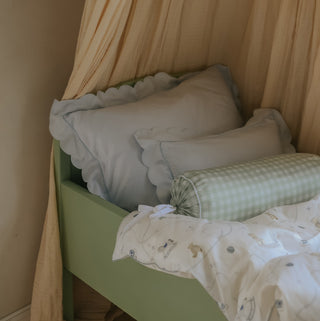 Green bed with decorative pillows and a picnic gingham green bolster pillow in a room with beige curtains.