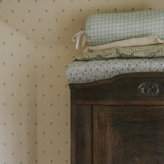 Wooden dresser with picnic gingham green bolster pillow and floral fabric on a patterned wall background