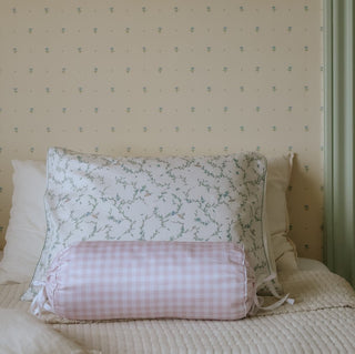 Floral-patterned pillow and checkered bolster on a bed with patterned wallpaper.