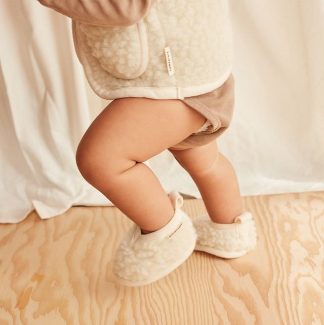 Child wearing booties on a wooden floor with a neutral background
