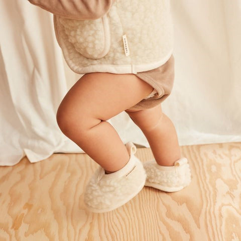 Child wearing booties on a wooden floor with a neutral background