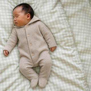 A sleeping newborn baby wearing a light taupe knit hooded footed cover up, lying on a picnic gingham green baby duvet