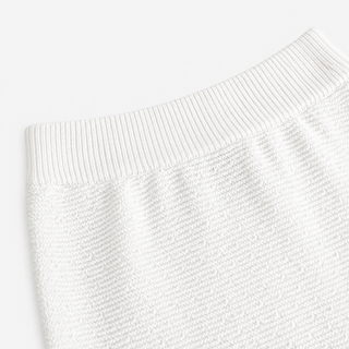Close-up of a white ribbed knit garment, showing the texture and waistband detail against a clean white background.