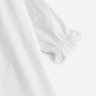 Close-up of a white textured fabric garment with a gathered elasticized cuff, shown against a plain white background.