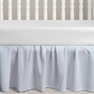 Blue crib skirt on a crib with a neutral background