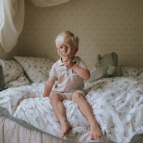 Dino Dreams Twin Set in Sage with little boy sitting on bed playing with a magnifying glass
