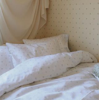 Neatly made bed with white bedding featuring a subtle pattern, against a light-colored wall.