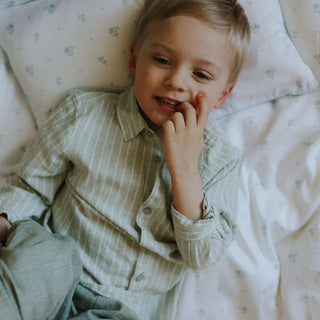 Child in a green shirt lying on a floral-patterned bed