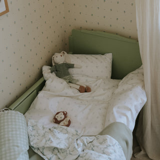 Child's bed with white bedding and teddy bears in a room with patterned wallpaper.