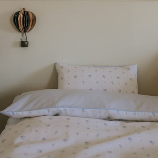 Bed with white bedding and a decorative pillow against a plain wall.