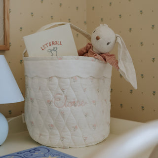 Quilted baby basket with plush toy and 'Let's Roll' book against a patterned wall.