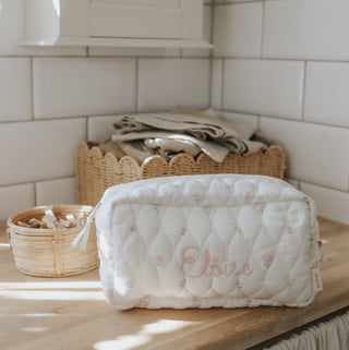 Quilted pouch with 'Eloise' embroidery on a wooden surface with baskets in the background.