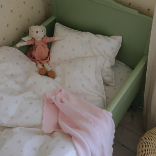 Small green bed with pink blanket and stuffed bunny toy against a patterned wall.